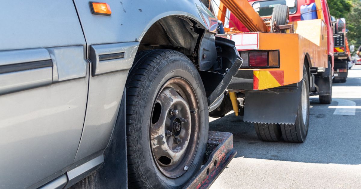 Tow truck towing an old car for removal.